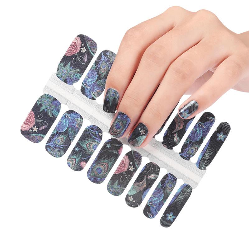 Hand wearing peacock print nail wraps with blue green feather pattern at-home manicure