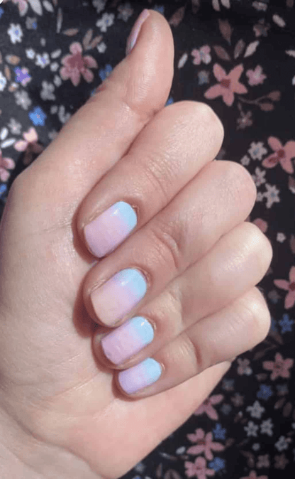Hand against floral background showing blue pink ombre nail wraps gradient manicure