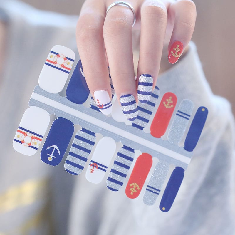 Hand wearing nautical nail wraps featuring red anchors blue stripes and white maritime nail art designs