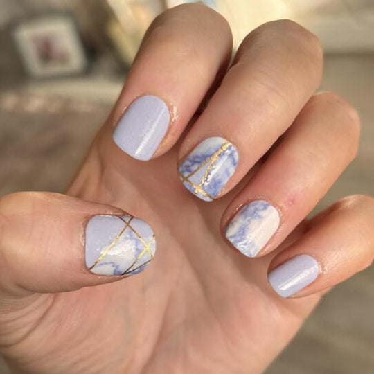 Blue marble nail wraps with gold geometric lines on hand showing at-home manicure