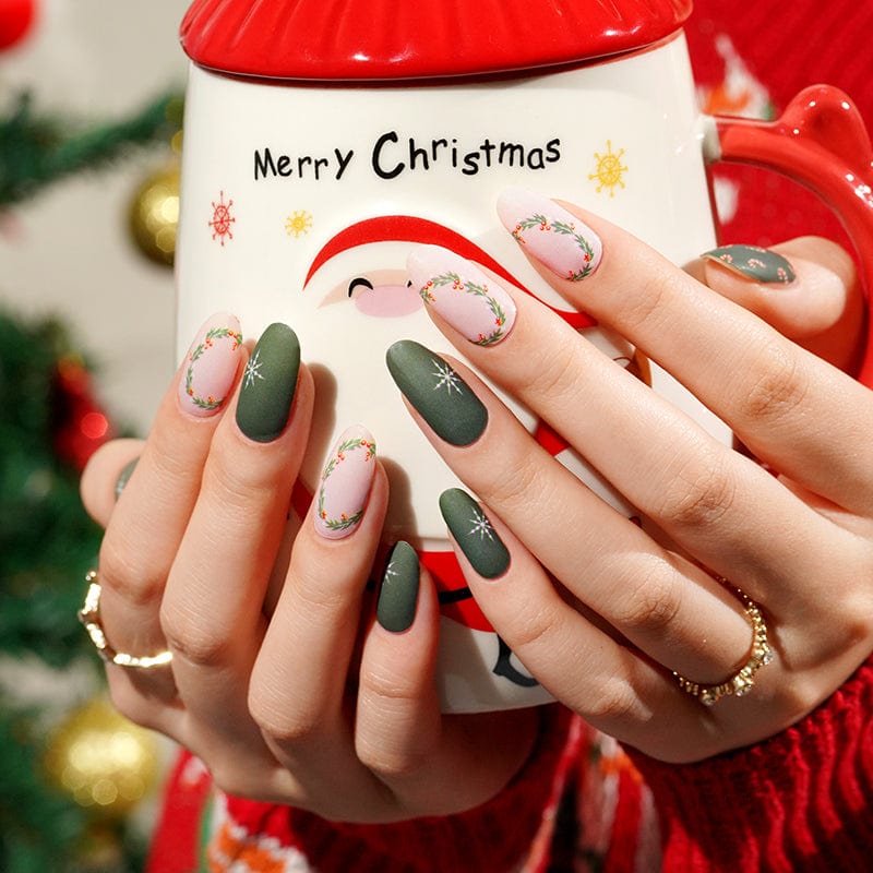 Green and pink Christmas nail wraps with holly patterns on hand holding festive mug