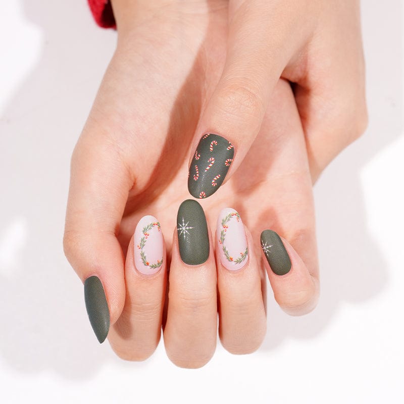 Hand wearing green and pink Christmas nail wraps with holly wreaths holiday nail art design
