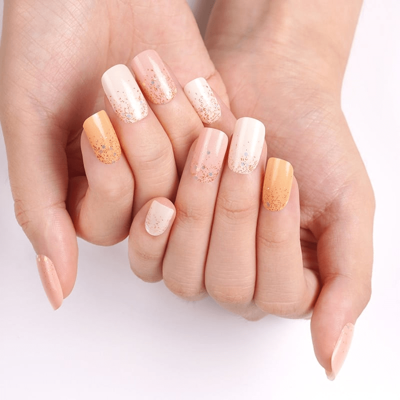 Hands wearing orange and cream glitter nail wraps with metallic gradient finish