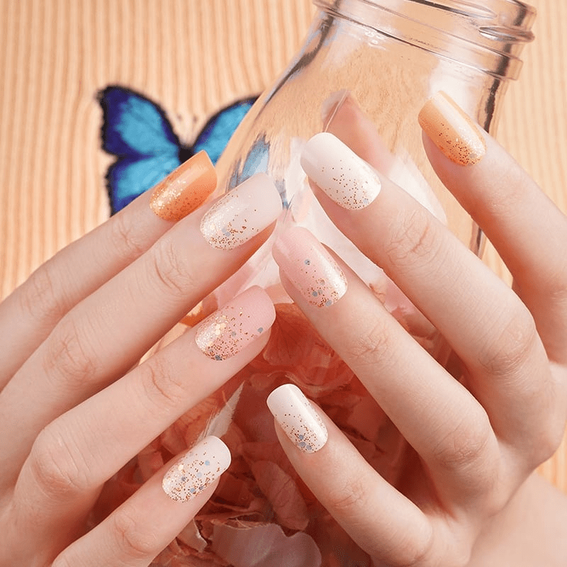 Hands holding glass jar showcasing orange glitter nail wraps with ombre effect