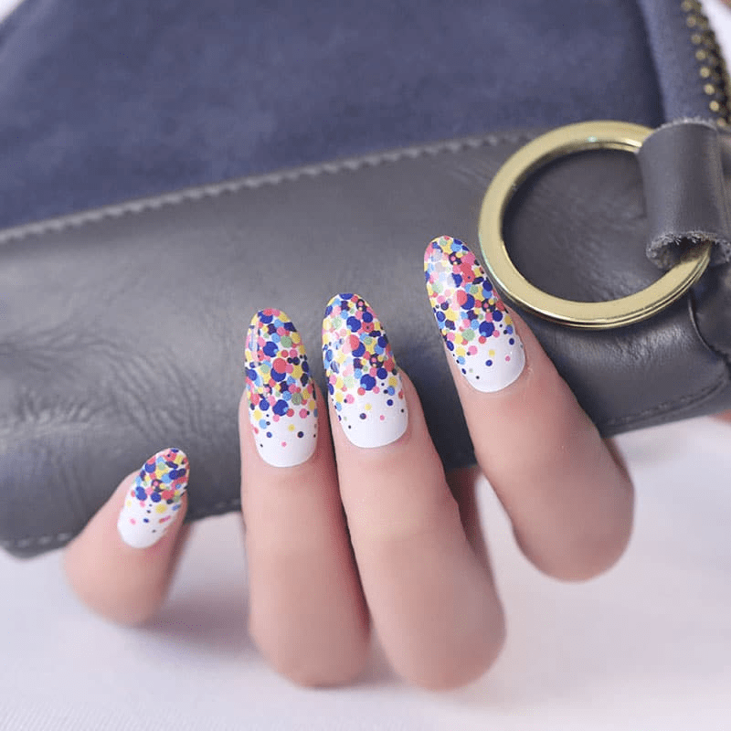 Manicured hand wearing colourful confetti polka dot nail wraps with rainbow spots