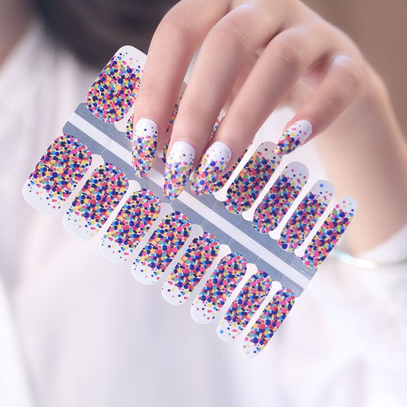 Hand holding multicoloured confetti nail wraps sheet with rainbow polka dot pattern