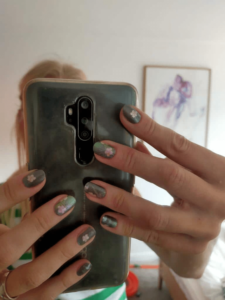 Close-up of tropical green nail wraps with hummingbird pattern on hands holding mobile phone