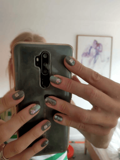Close-up of tropical green nail wraps with hummingbird pattern on hands holding mobile phone
