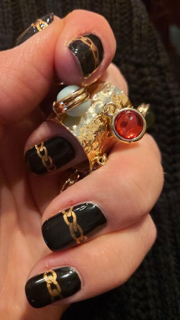Black nail wraps with gold chains on hand wearing statement rings luxe manicure