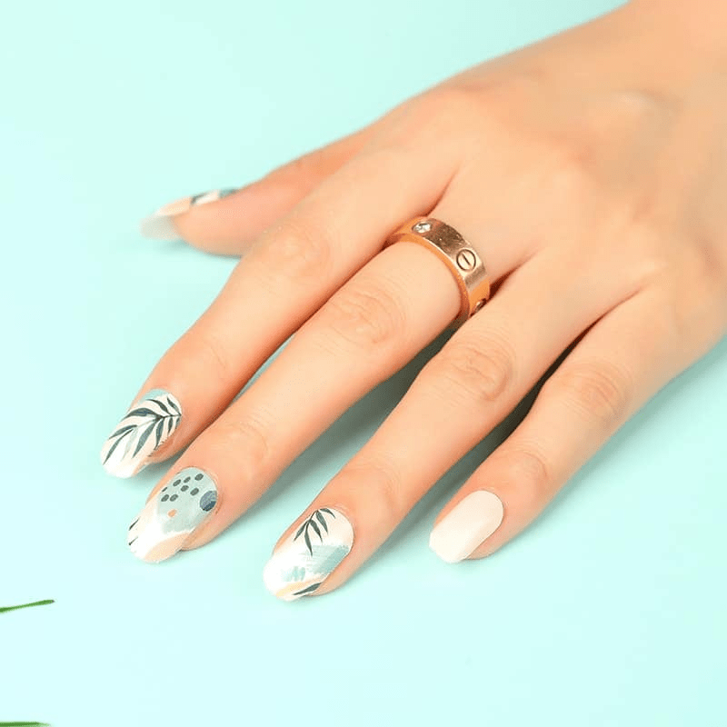 Natural botanical nail wraps on hand featuring black leaf designs and neutral beige finish