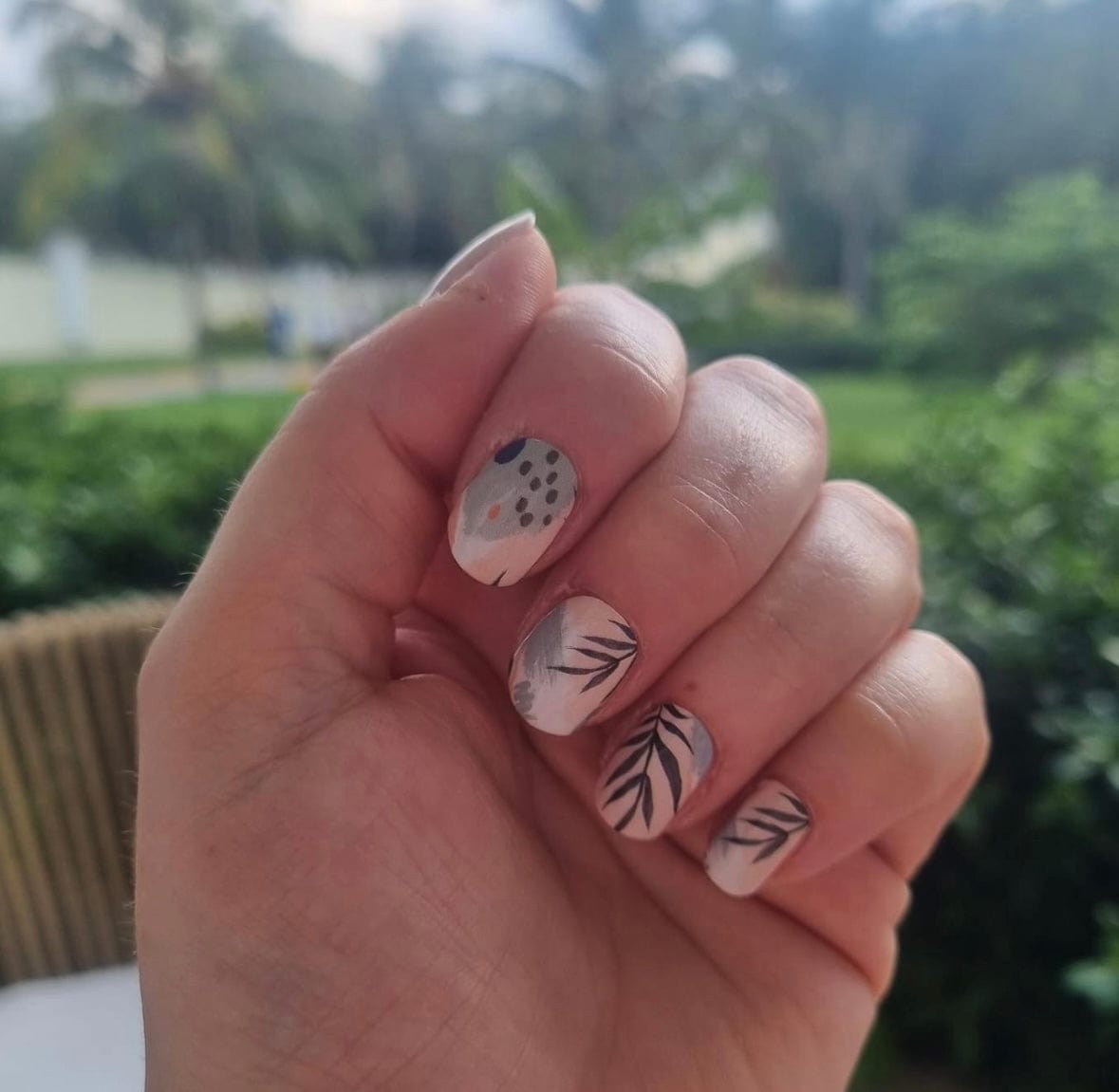 Hand displaying botanical nail art with black leaf patterns on neutral matte finish nail wraps