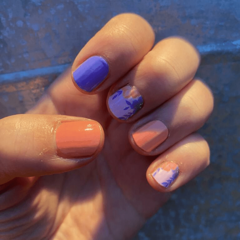 Hand wearing purple and coral nail wraps with pink floral accent nail art