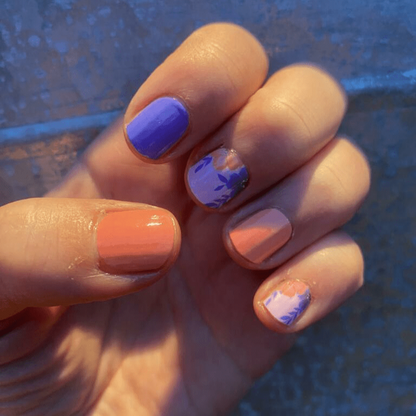 Hand wearing purple and coral nail wraps with pink floral accent nail art