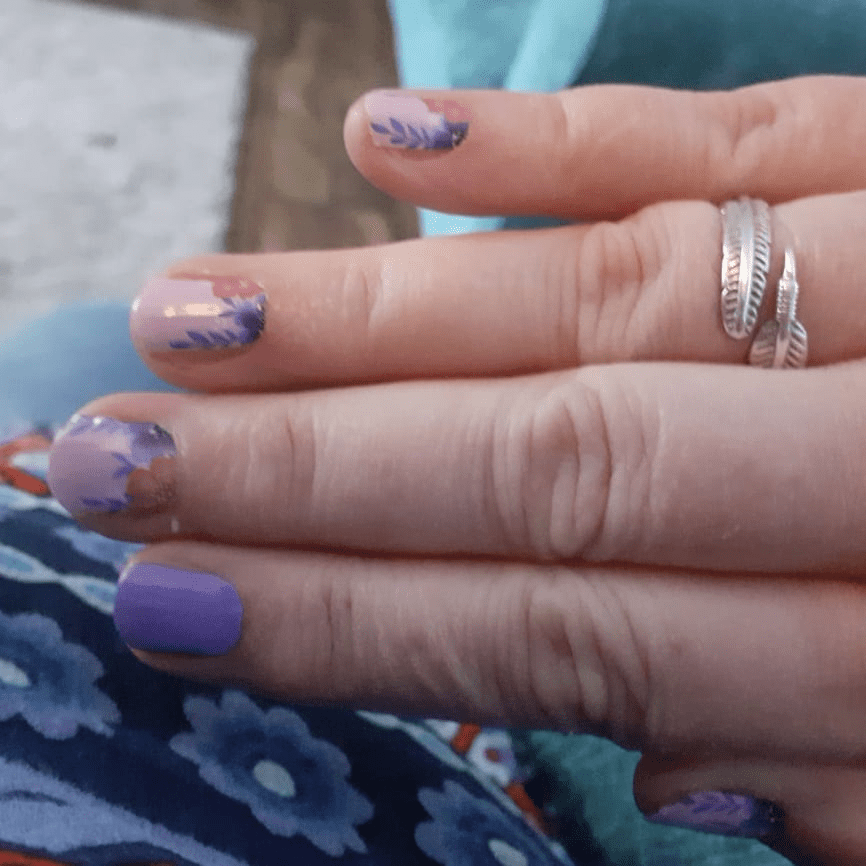 Hand with silver rings showing floral nail wraps in purple and pink tones