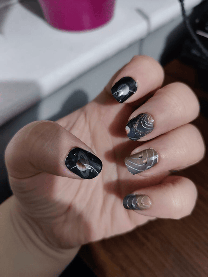 Black and silver chrome nail wraps on hand with metallic geometric patterns for at-home manicure