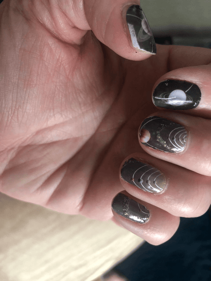 Glossy black nail wraps with chrome silver geometric details on hand showing reflective finish