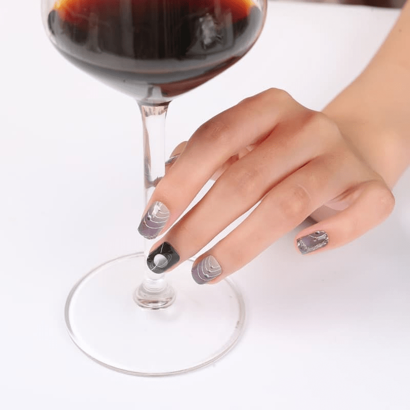 Hand holding wine glass wearing silver chrome geometric nail wraps with space-themed patterns