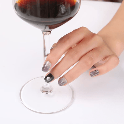 Hand holding wine glass wearing silver chrome geometric nail wraps with space-themed patterns