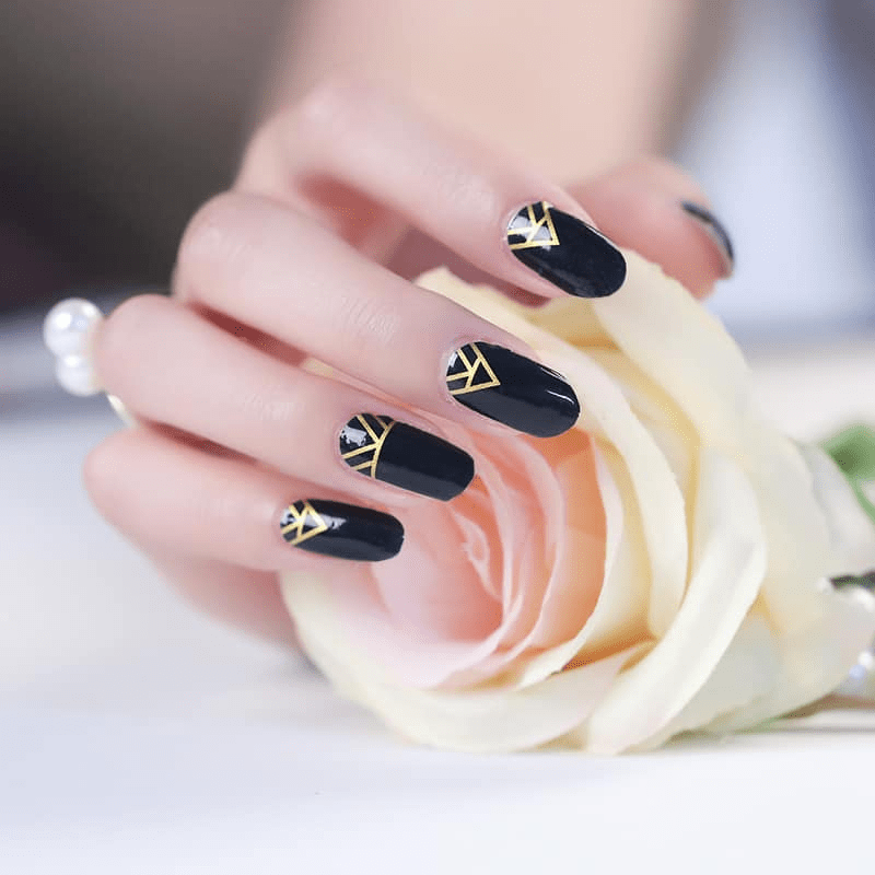 Hand with white rose showing black and gold geometric nail wraps art deco design