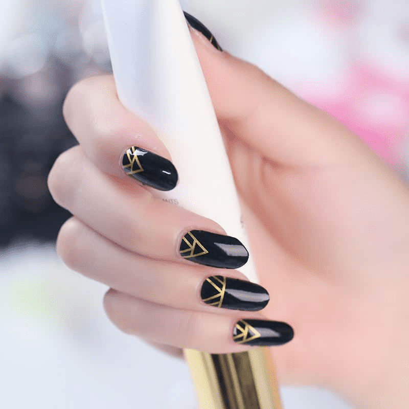 Black nail wraps featuring gold triangular geometric patterns elegant art deco manicure on hand