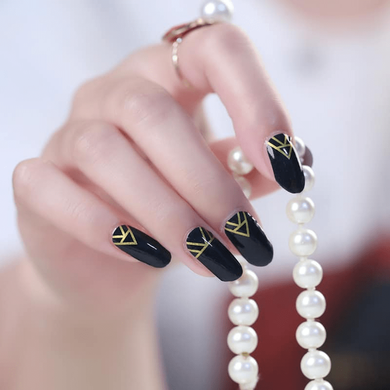 Black glossy nail wraps with gold geometric art deco line accents at the cuticle