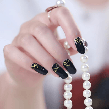 Black glossy nail wraps with gold geometric art deco line accents at the cuticle