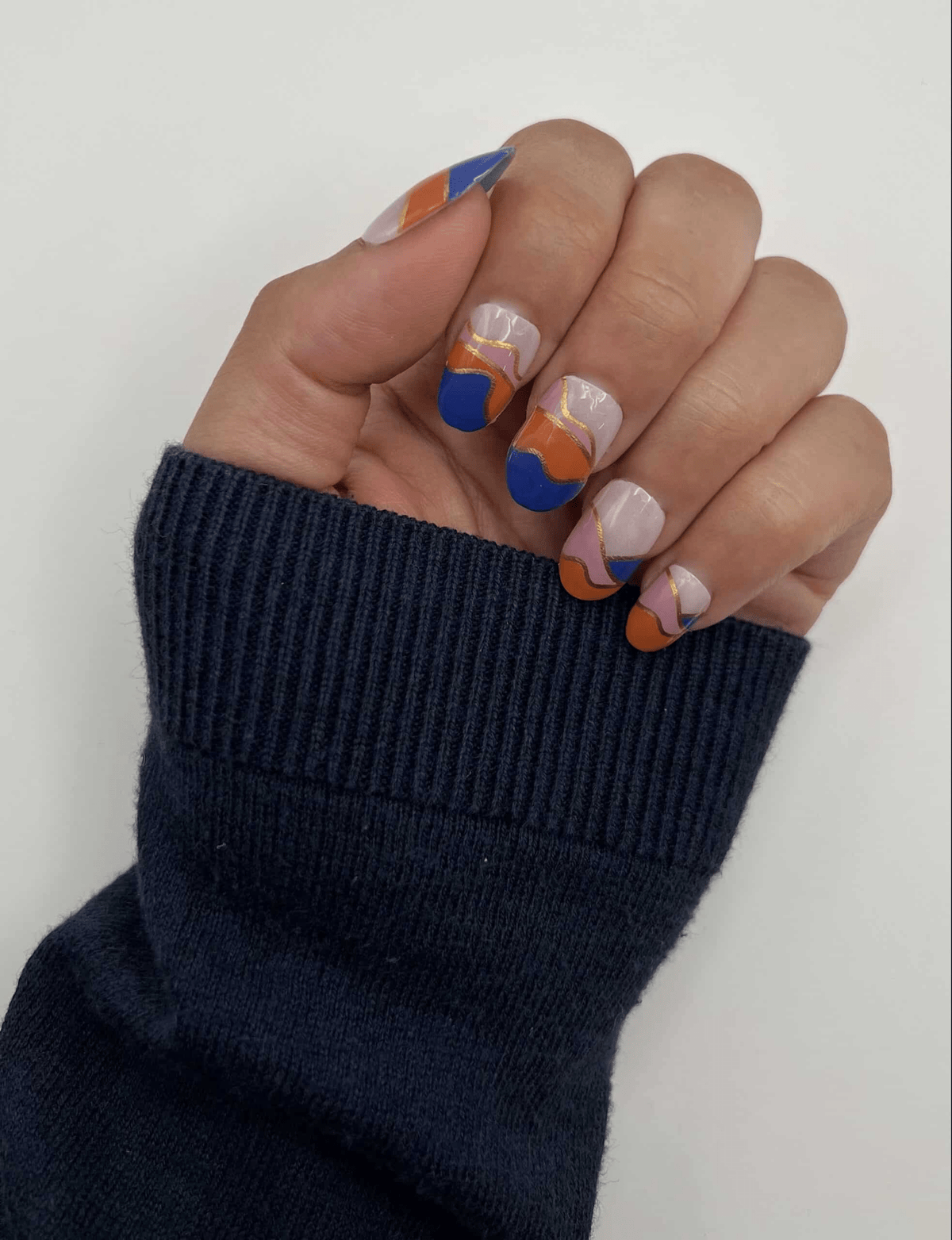 Hand modelling multicoloured nail wraps with navy blue coral geometric wave patterns