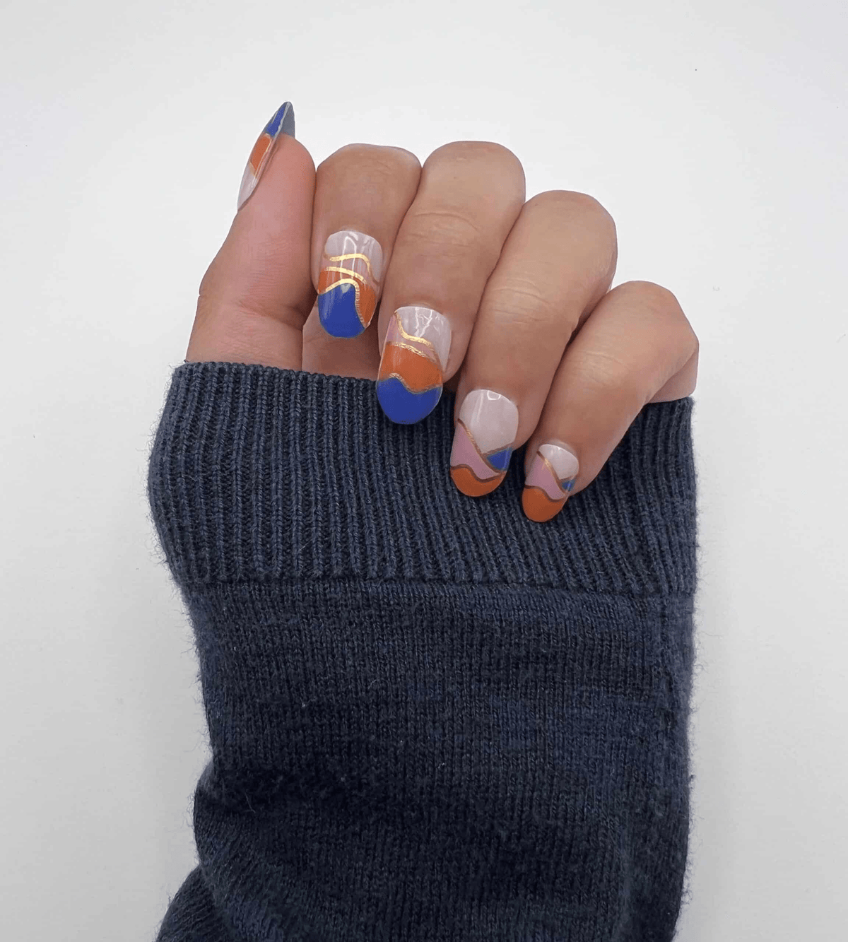 Hand displaying abstract nail wraps with blue orange pink geometric colour blocking design