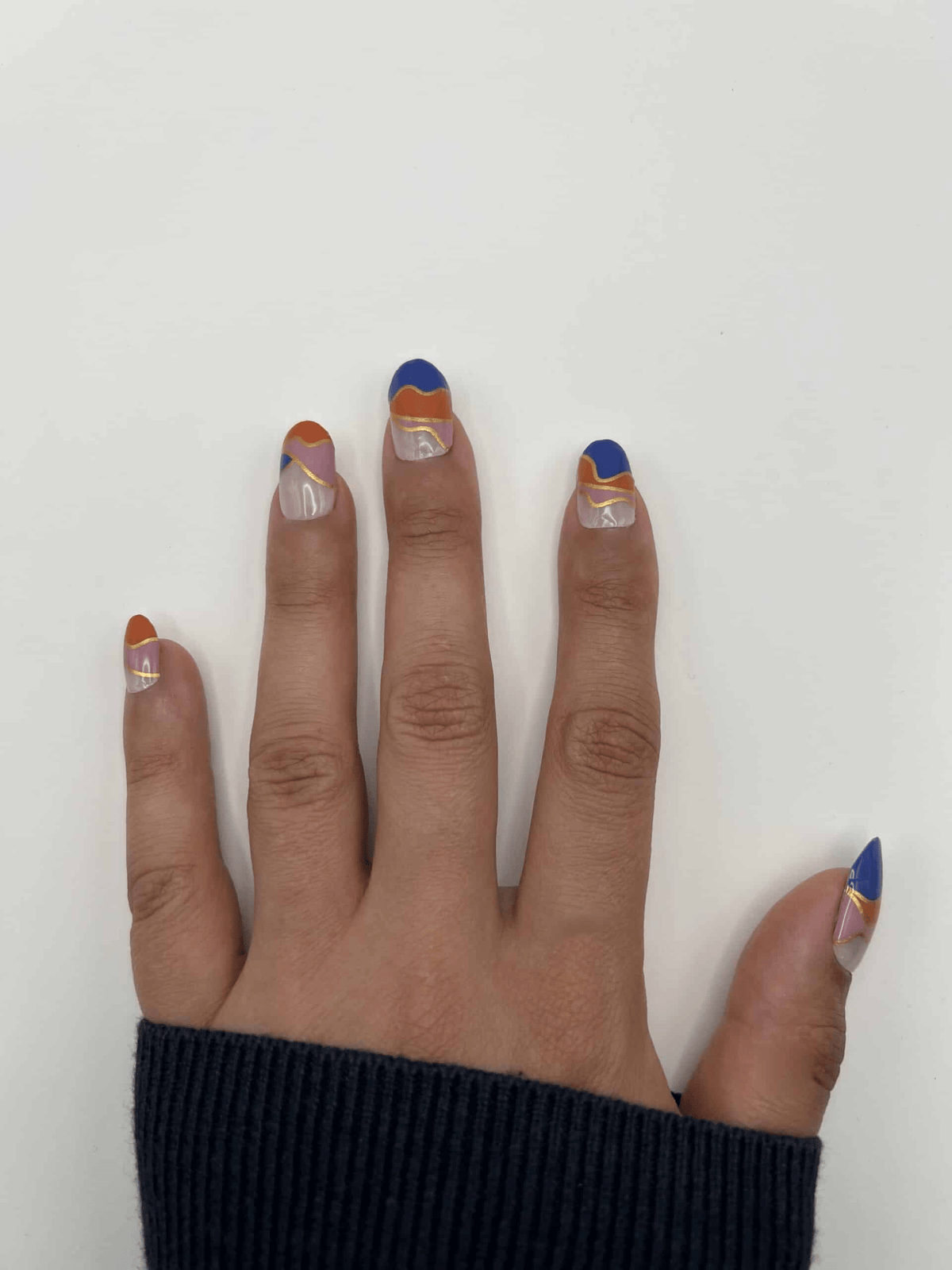 Hand wearing geometric non-UV nail wraps in navy blue, coral orange and nude colour block design