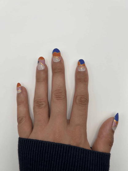 Hand wearing geometric non-UV nail wraps in navy blue, coral orange and nude colour block design