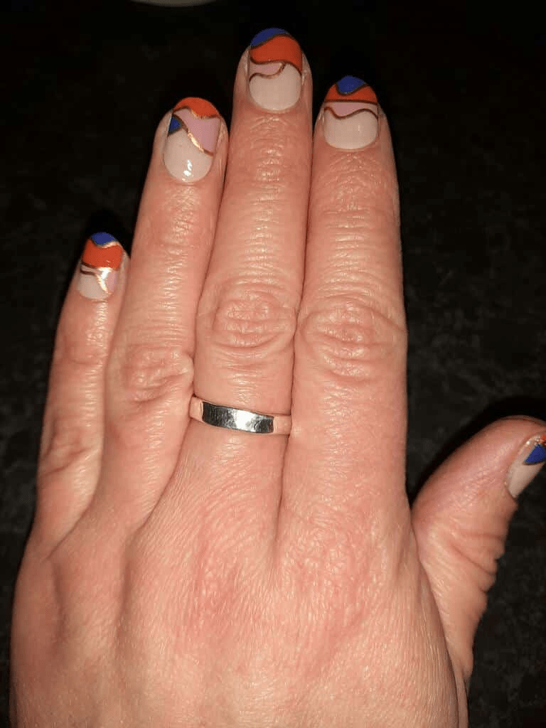 Hand with wedding ring displaying geometric nail wraps in navy blue, orange and nude design