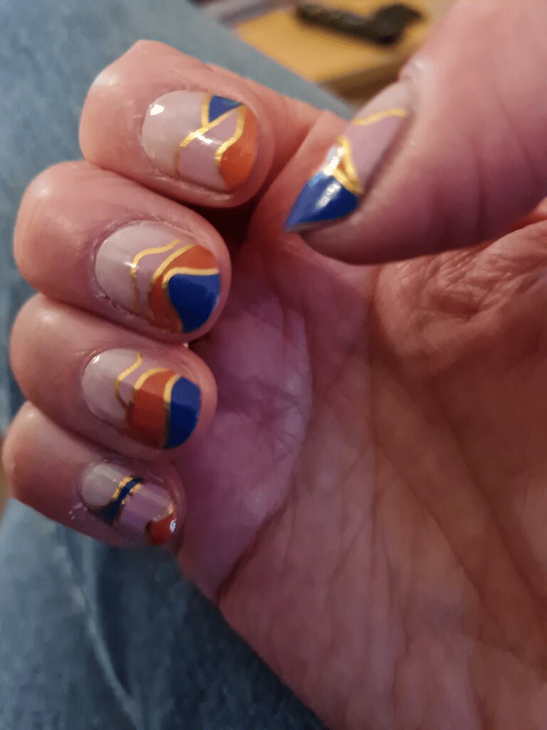 Close-up hand showing colourful geometric nail art wraps in blue, coral and nude tones