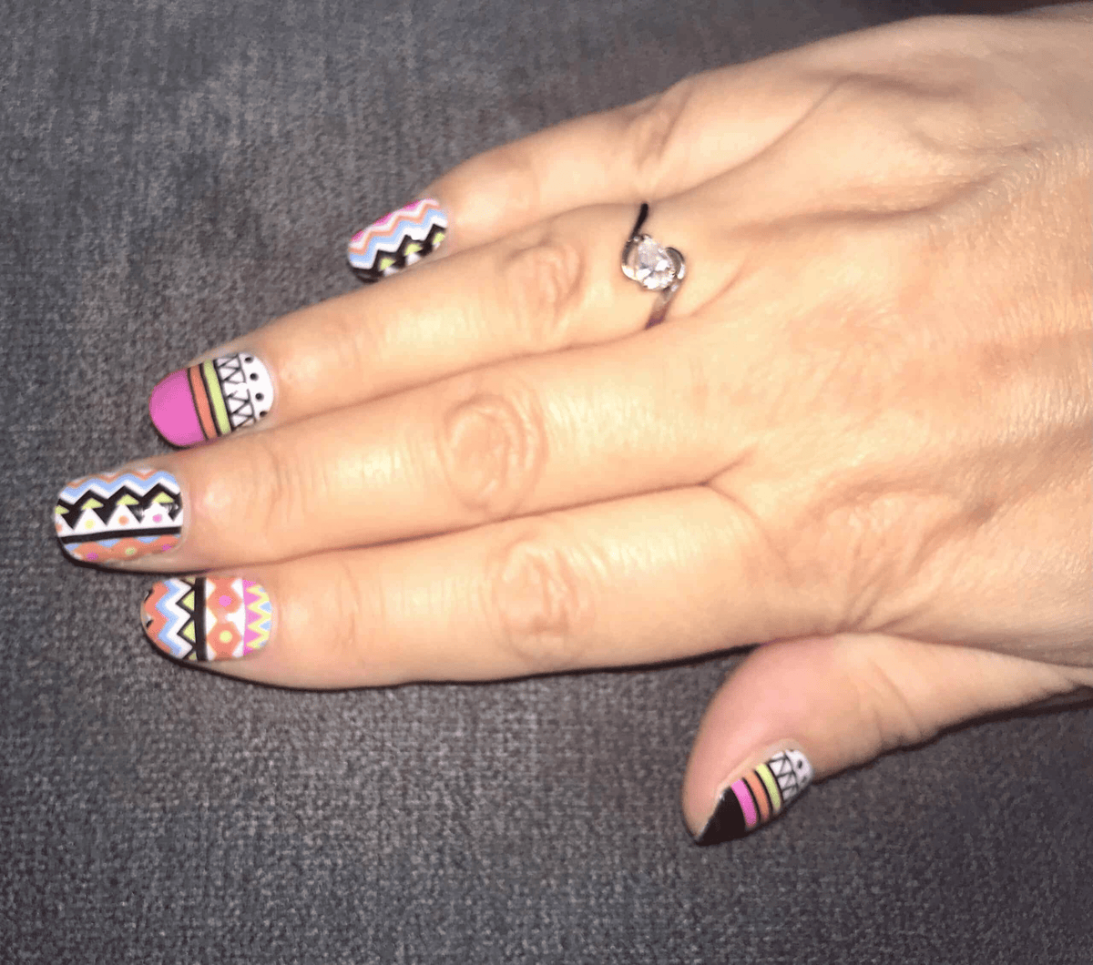 Hand wearing multicoloured tribal chevron nail wraps with geometric patterns and stripes