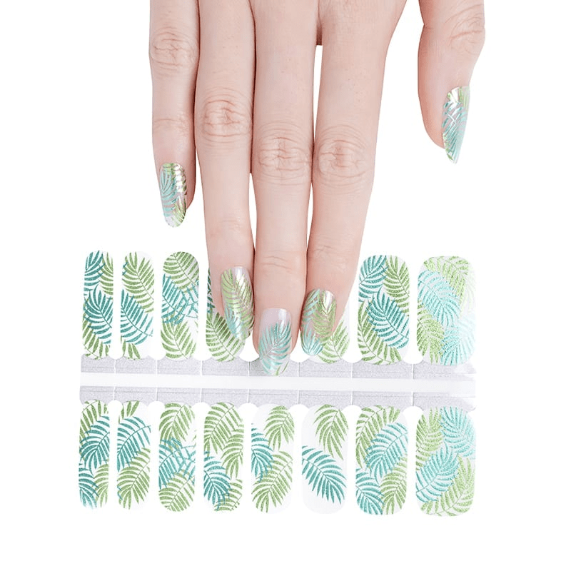 Hand applying green botanical fern nail wraps with sheet showing tropical leaf patterns