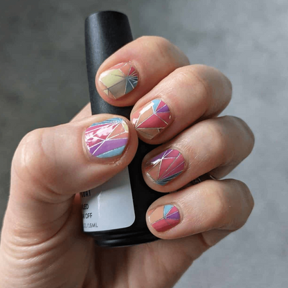 Hand holding nail polish bottle wearing multicoloured geometric kaleidoscope nail wraps with prism pattern