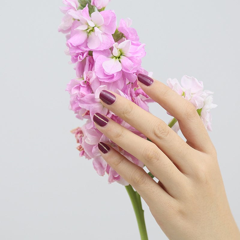 Deep burgundy nail wraps with subtle shimmer and fine gold vertical stripe accent