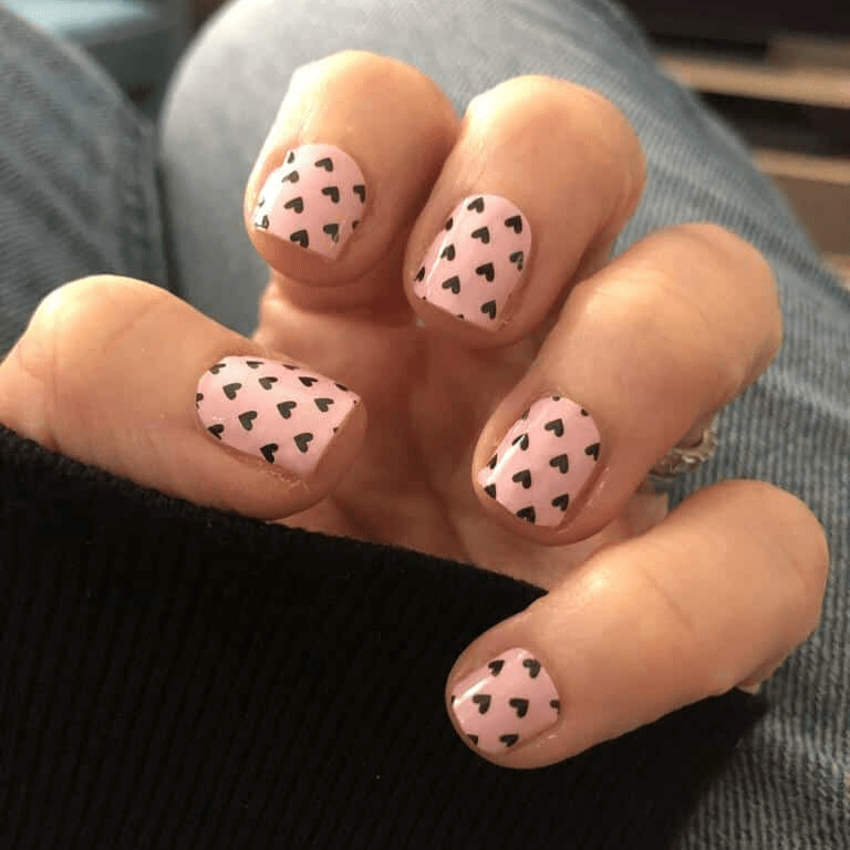 Pink nail wraps with black heart pattern on hand showing romantic manicure design
