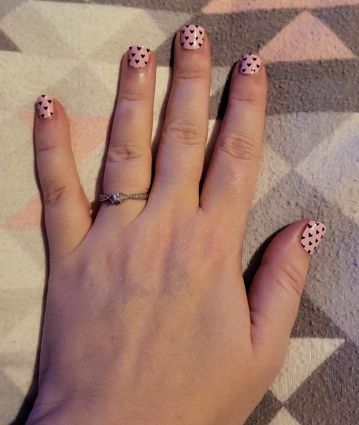 Hand wearing pink nail wraps with black heart pattern showing cute romantic manicure
