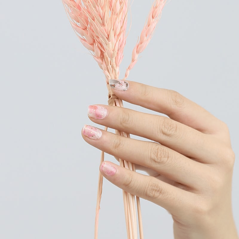 Hand holding dried flowers wearing pink koi fish nail wraps with watercolour finish