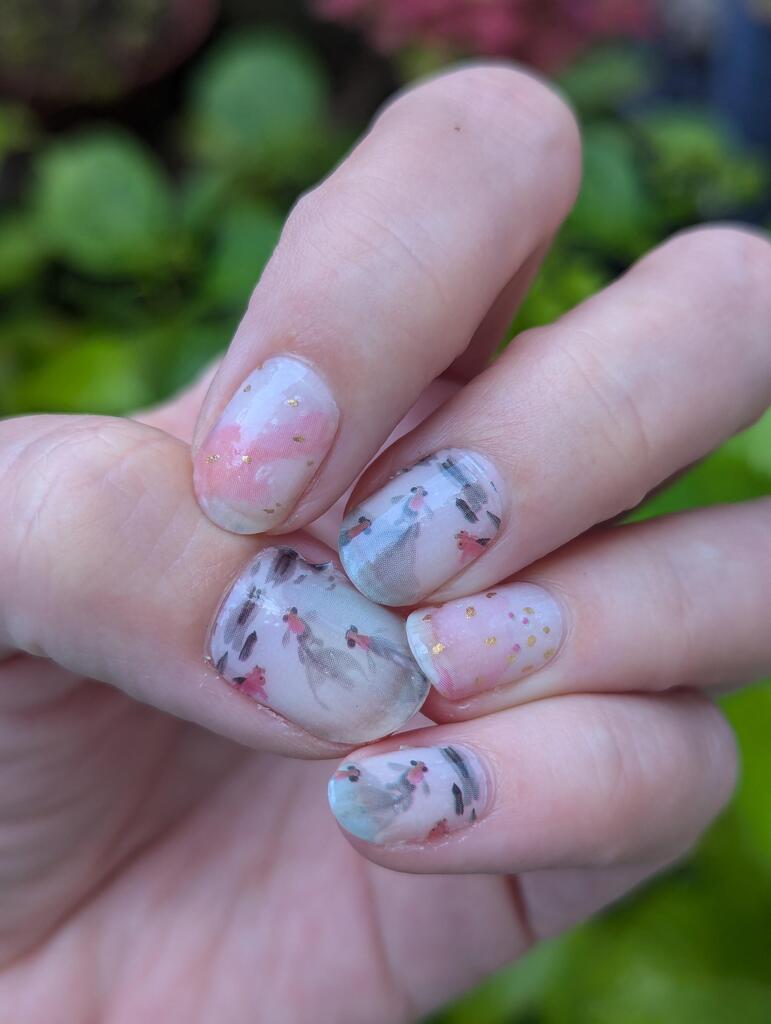 Hand wearing koi fish nail wraps with pink and grey watercolour pattern