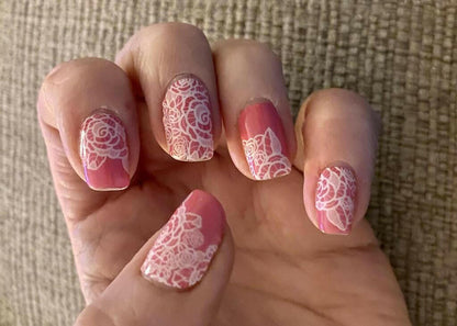 Close-up of pink floral nail wraps featuring intricate white lace rose patterns on fingertips