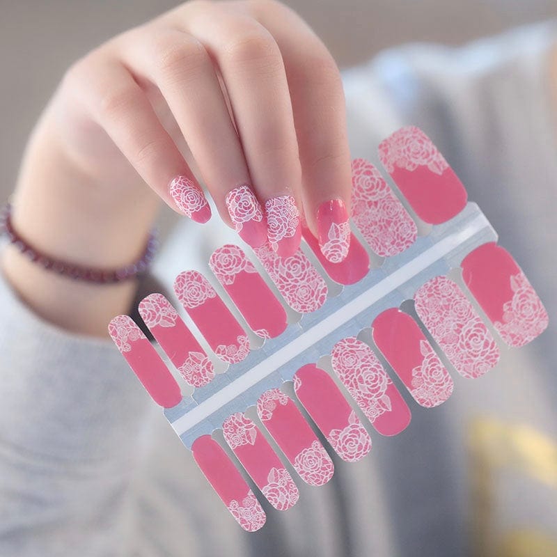 Hand holding pink rose lace nail wraps sheet displaying delicate floral patterns for manicures