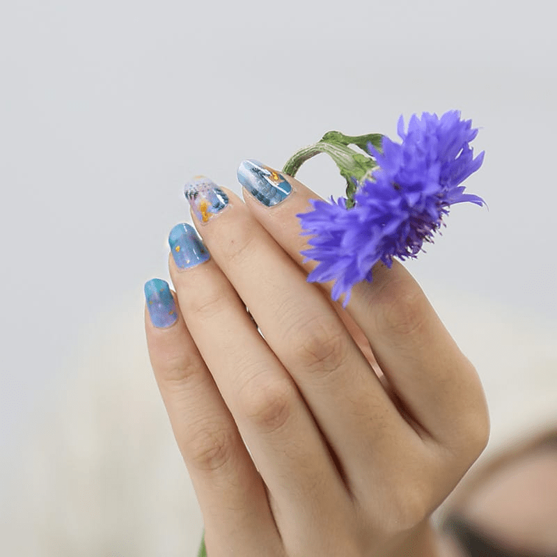 Hand wearing blue floral nail wraps holding purple flowers for spring manicure