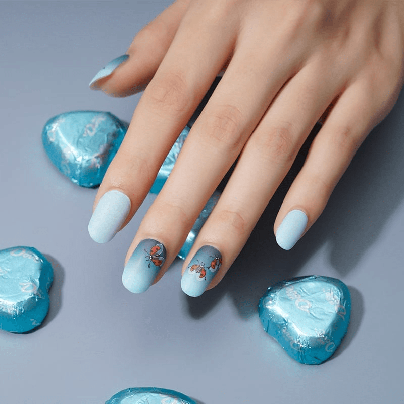 Hand with light blue nail wraps decorated with ladybird nail art design