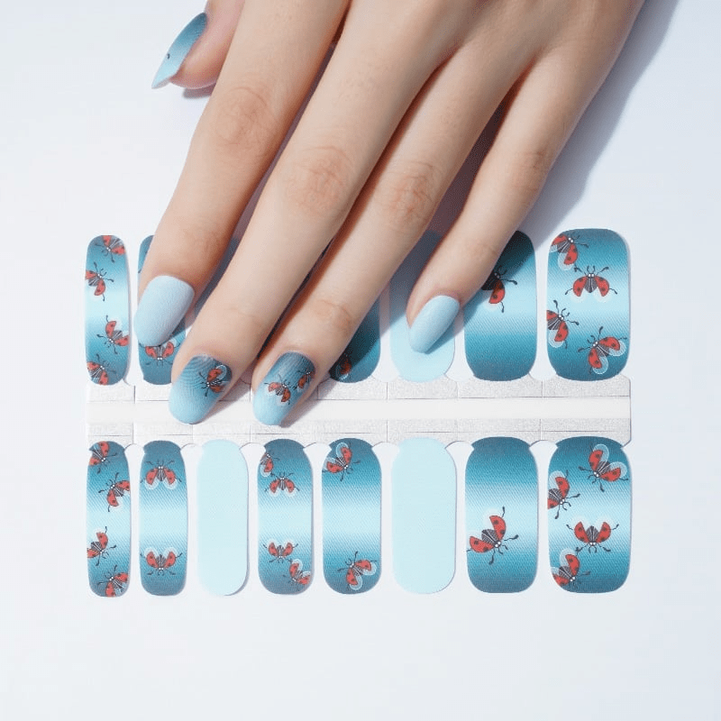 Blue nail wraps with red ladybird pattern applied on hand showing cute cottagecore nail art