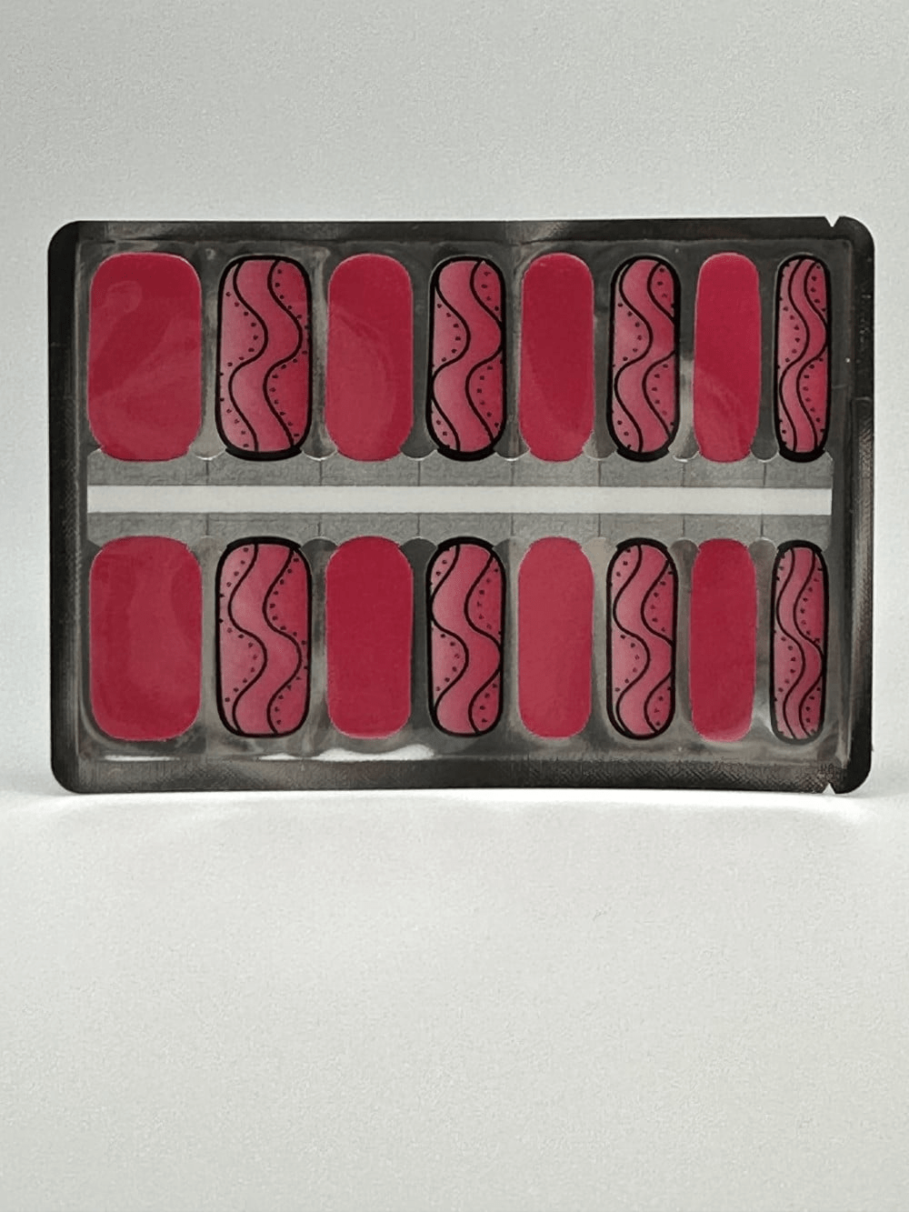 Pink nail wraps with black swirl patterns displayed in application sheet packaging