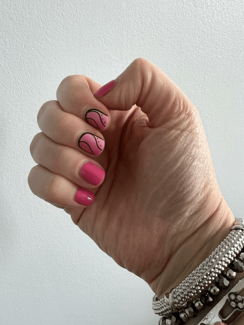 Hand wearing hot pink nail wraps with black swirl patterns on glossy finish