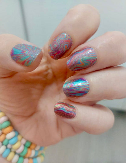 Hand displaying colourful nail wraps with psychedelic swirl patterns in rainbow hues