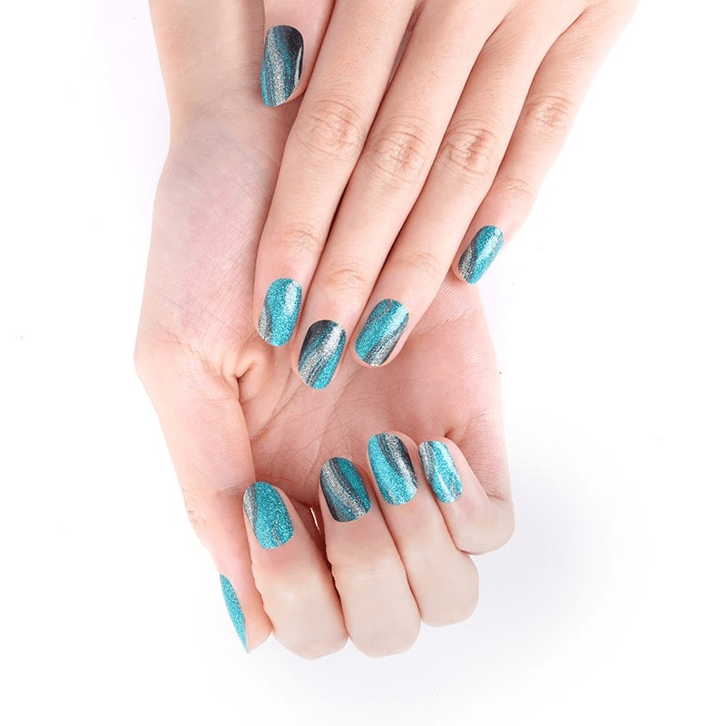 Hands displaying teal gold glitter nail wraps with metallic reptile pattern effect