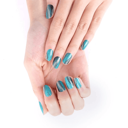 Hands displaying teal gold glitter nail wraps with metallic reptile pattern effect